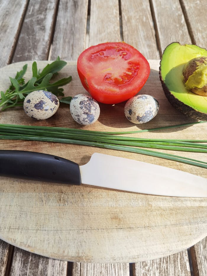 A rustic setup featuring fresh avocado, tomato, quail eggs, and chives for a natural culinary shot.
