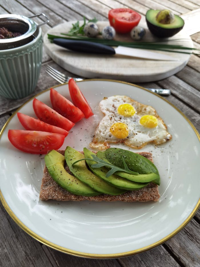 Delicious breakfast plate featuring avocado toast and fried quail eggs with fresh tomatoes.
