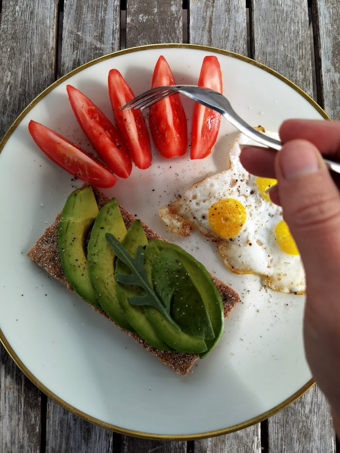 Top view of avocado toast with fried eggs and tomatoes on a rustic table.